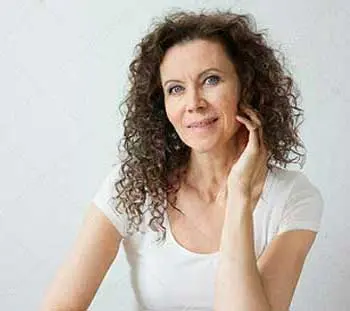 Primer plano de Miriam en un fondo gris y camiseta informal blanca.